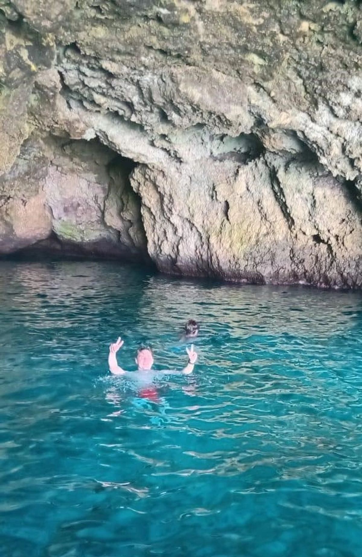 Guests swimming in clear blue water beside a rocky cave